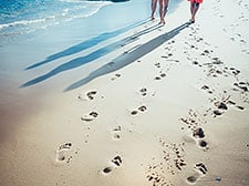 A beach with footprints and the shadows of three people